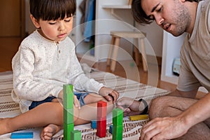 Kid and his father playing at home with wood building blocks. Homeschooling. Stay at home. Family time