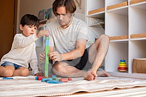 Kid and his father playing at home with wood building blocks. Homeschooling. Stay at home. Family time