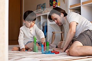 Kid and his father playing at home with wood building blocks. Homeschooling. Stay at home. Family time