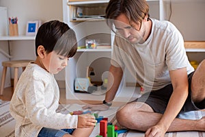 Kid and his father playing at home with wood building blocks. Homeschooling. Stay at home. Family time