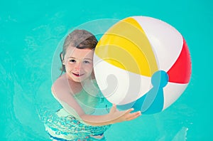 Kid hold rubber air ball in pool. Happy child having fun on summer vacation. Kid playing with ball in the swimming pool