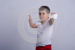 Kid holding discount white card in  hand. Kid with credit card. Little boy showing empty blank paper note copy space.