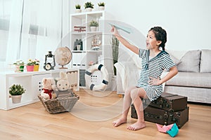 Kid holding a paper plane sitting on the suitcase.