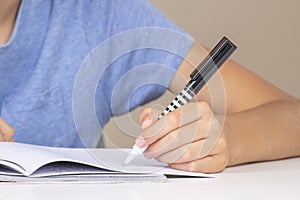 Kid holding pen in left hand and doing homework, writing in open notebook. Left Handers Day