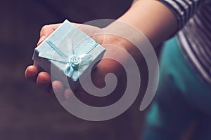 Kid holding a small blue gift box with ribbon in his hand