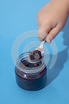 Kid holding spoon under Jar of Blackberry. Selective focus