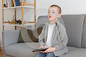 Kid holding TV remote controller. Boy without parental control watching television