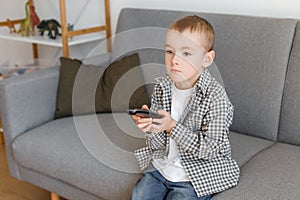 Kid holding TV remote controller. Boy without parental control watching television