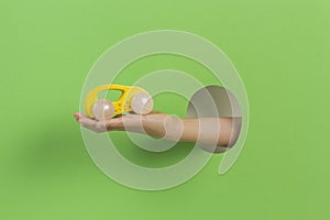 Kid holding yellow wooden toy car in hand through hole on light green background