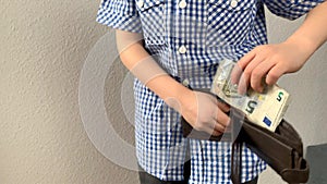 Kid holds euro banknotes in his hand and puts them in a brown wallet, concept of pocket money, theft, shopping