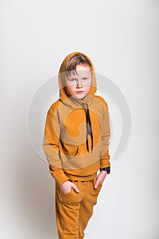 Kid in hood from yellow fashion sport suit hoodie. Blond kid face in a hood looks from under a forehead. Stylish child