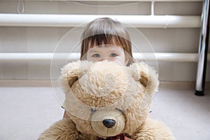 Kid hugging teddy bear indoor in her room, devotion concept, child behind toy