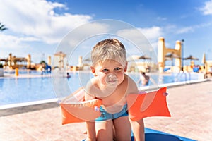 Kid with inflatable armbands near swimming pool.