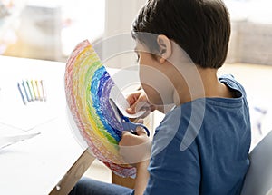 Kid is isolation using scissors cutting paper in rainbow shape on white background, Children activities at home while school off.