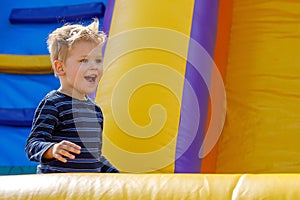 Kid jump in inflatable bounce castle on kindergarten birthday party. Activity and play center for young child. Little smiling boy