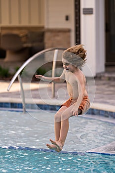 Kid jumping in swim pool. Child splashing in summer water pool. Kid splash in pool. Excited happy kid boy jumping in