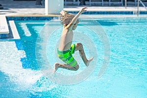 Kid jumping in water pool. Kid enjoying summer holiday, swiming in pool. Kid having fun on summer holidays at pool