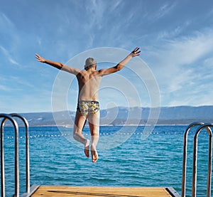 The kid jumps from the dock into the sea copy space image