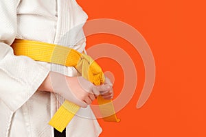 Kid in karate kimono holding his yellow belt, close up. Boy practicing karate on color background, copy space