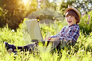 Kid with a laptop outdoors in the summer. Ð¡hild in a park on distance learning. Online communication with relatives and friends.
