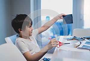 Kid learning how to use the scissors cut the paper,Schoolboy using scissors cutting black paper in square shape,Child showing art