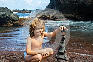 Kid learning sort or stack pebble stone tower or pyramid on water for balance, training and meditation with nature, kids