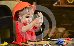 Kid learning to use screwdriver. Concentrated kid in orange helmet working in workshop. Future occupation concept