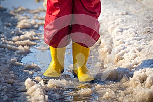 Kid legs in rainboots standing in the ice puddle photo