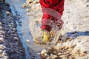 Kid legs in rainboots jumping in the ice puddle photo