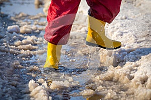 Kid legs in rainboots running in the ice puddle