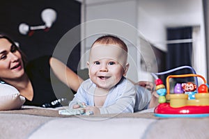 The kid lies on a bed with mother and ridiculously smiles