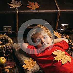 Kid lies laying hands behind head and resting on wooden floor in golden leaves. Biggest discounts for all autumn clothes