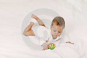 The kid lies in a snow-white bed, laughs and plays with a rattle.