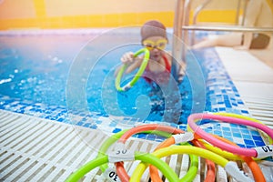 Kid little girl learning to underwater swim pool with ring with coach woman