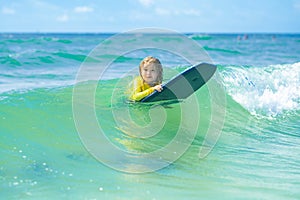 Kid little surfer learn to ride on surfboard on sea waves. Happy child playing in the sea. Kid having fun at the beach