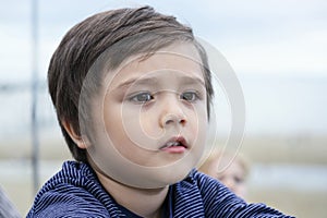 The kid lost in thought looking out withblurry sea view background, Side view portrait of  little boy deep in thoughts. Close up t