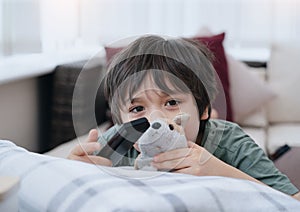 Kid lying on sofa looking at camera with smiling face, Cute boy laying down on couch holding remote, Child watching TV relaxing at