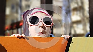 Kid makes faces and has fun on playground, little girl plays outdoors in spring. Portrait of funny playful child in sunglasses