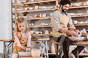 kid making ceramic pot on pottery wheel with teacher