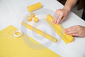 Kid making natural rolled beeswax candle from pressed beeswax honeycomb sheet at home indoors.