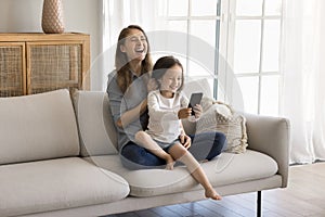 Kid and mom laugh sit on sofa with smartphone