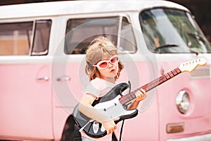 Kid musician playing the guitar like a rockstar on pink background in neon light. Cute pupil having music lesson. Cute