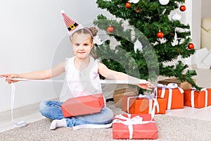 Kid opening Xmas presents. Child under Christmas tree with gift boxes