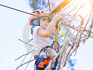 Kid in orange helmet climbing in trees on forest adventure park. Girl walk on rope cables and high suspension bridge in