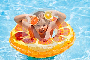 Kid with orange in the pool. Summer fruits. Child boy in swimming pool. Little kid boy having fun in the pool. Outdoor