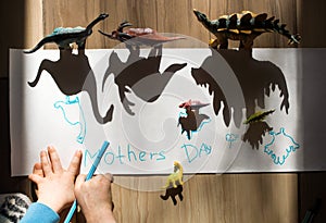 Kid outlines the shadows of large and small dinosaur toy figures