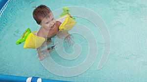 Kid in oversleeves swims in the pool in the yard