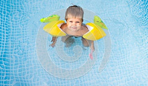 Kid in oversleeves swims in the pool in the yard