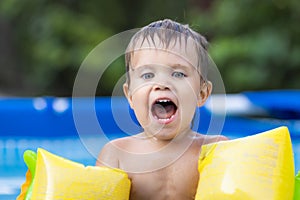 Kid in oversleeves swims in the pool in the yard
