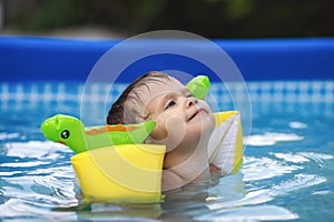 Kid in oversleeves swims in the pool in the yard